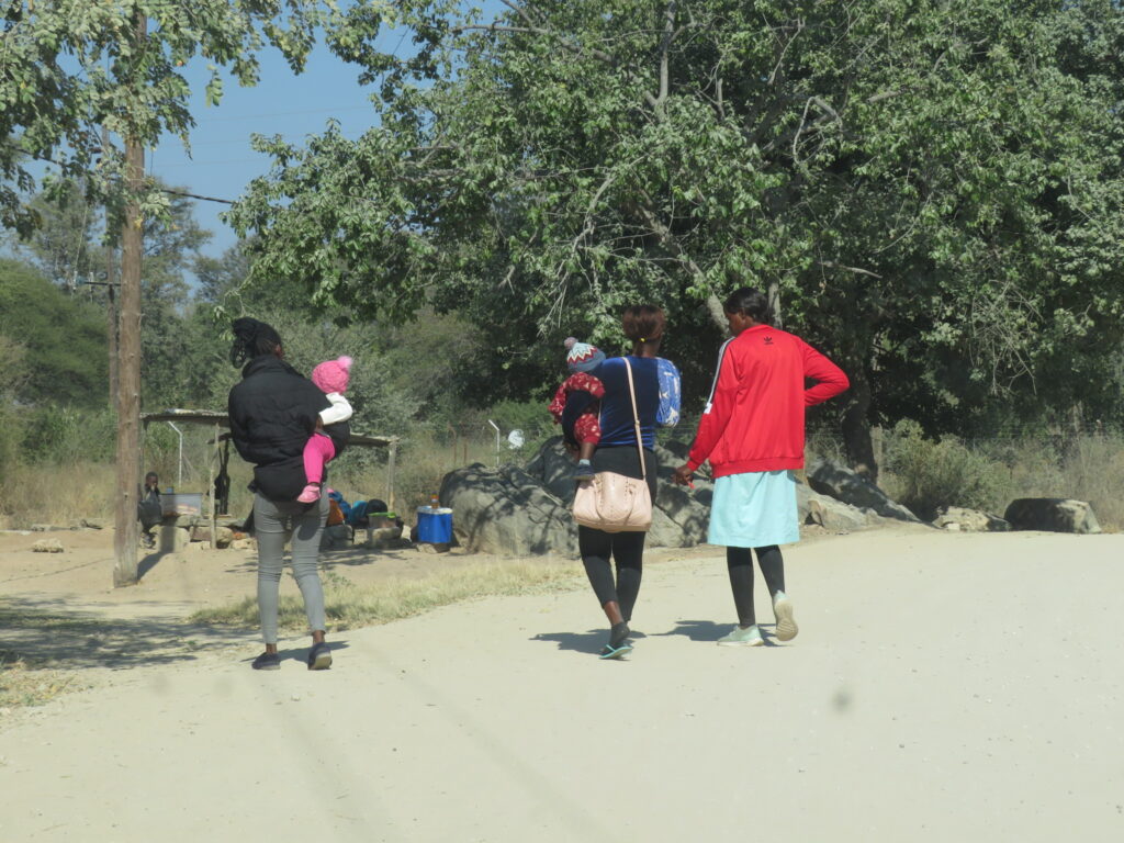 Three young women are walking away from the camera. Two carry toddlers on their hip.