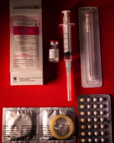 A collection of various contraceptive methods (the patch, the injection, male condoms, the pill) on a deep red background