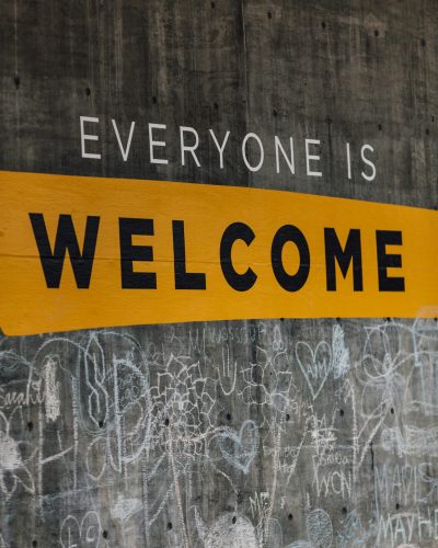 A grey concrete wall with the words "Everyone Is Welcome" printed in capital letter